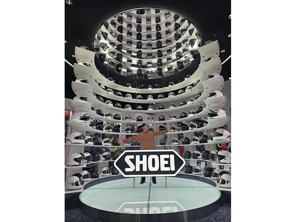 SHOEIヘルメットパーク2階展示コーナーのヘルメットタワーと浦崎さん